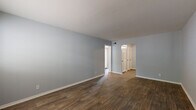 This single-floor, 2-bedroom, 2-bathroom residence offers a clean and modern living environment with consistent design throughout. The living room provides an open, airy feel with rich dark wood-style flooring, soft blue-gray walls, and white trim that creates a bright, neutral palette. A front-facing window allows natural light to fill the space. The kitchen is well-equipped with white shaker-style cabinetry, granite countertops, subway tile backsplash, stainless steel appliances including a gas range, and wood-style flooring that complements the rest of the unit. Both bathrooms feature granite-topped white vanities, wood-style flooring, and clean white subway tile surrounds in the tub-shower combinations. The primary bedroom is generously sized, finished with soft carpeting and neutral walls. The second bedroom also features plush carpeting, a sliding-door closet for storage, and a window providing natural light and outdoor views. A connecting hallway links the bedrooms and bathrooms efficiently, contributing to the unit's practical floor plan. Throughout, the consistent use of soft blue-gray paint, white woodwork, and wood-style flooring creates a cohesive, move-in-ready aesthetic.