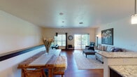 This single-floor residence offers a thoughtfully designed open-concept layout that seamlessly connects the dining and living areas. Rich hardwood flooring flows throughout the main living spaces, complementing the warm, neutral tones found on the walls and ceilings. The dining area features a sturdy wooden table, while the adjacent living room is anchored by a sectional sofa, a tufted ottoman, and a leather recliner, all centered beneath a large statement artwork. A sliding glass door opens to an outdoor deck, flooding the space with natural light and providing views of the surrounding greenery.

The kitchen is outfitted with dark espresso cabinetry, granite countertops, and a full suite of stainless steel appliances, including a refrigerator, range, and microwave. The space is efficiently arranged for both function and style.

Multiple bedrooms offer comfortable retreats, each carpeted and featuring windows that allow in natural light. The primary bedroom includes ample storage with a full dresser and armoire ensemble. Two full bathrooms serve the residence, both finished with dark cabinetry, granite vanity tops, and hardwood flooring, providing a cohesive and polished aesthetic throughout the home.