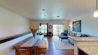 This single-floor residence offers a thoughtfully designed open-concept layout that seamlessly connects the dining and living areas. Rich hardwood flooring flows throughout the main living spaces, complementing the warm, neutral tones found on the walls and ceilings. The dining area features a sturdy wooden table, while the adjacent living room is anchored by a sectional sofa, a tufted ottoman, and a leather recliner, all centered beneath a large statement artwork. A sliding glass door opens to an outdoor deck, flooding the space with natural light and providing views of the surrounding greenery.

The kitchen is outfitted with dark espresso cabinetry, granite countertops, and a full suite of stainless steel appliances, including a refrigerator, range, and microwave. The space is efficiently arranged for both function and style.

Multiple bedrooms offer comfortable retreats, each carpeted and featuring windows that allow in natural light. The primary bedroom includes ample storage with a full dresser and armoire ensemble. Two full bathrooms serve the residence, both finished with dark cabinetry, granite vanity tops, and hardwood flooring, providing a cohesive and polished aesthetic throughout the home.