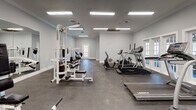 Located at 500 Hambrick Rd in Stone Mountain, Georgia, this fitness center offers a well-appointed, single-floor workout facility designed to support a full range of exercise routines. The space features soft gray walls, crown molding, and durable rubber-floored workout areas that provide both a clean aesthetic and a functional environment for exercise.

The main workout area is generously sized and equipped with multiple Landice treadmills, elliptical machines, and other cardio equipment, providing ample room for users to work out comfortably. Strength training is well-represented through a selection of Paramount and Nautilus cable and weight machines, a multi-station functional trainer, adjustable benches, and a full rack of Hex dumbbells ranging across various weights.

Large French doors and windows line the walls, allowing natural light to pour into the space and offering views of the outdoor pool area, creating an open and inviting atmosphere. Overhead, rows of recessed fluorescent panel lighting ensure bright, even illumination throughout. A wall-mounted television is also present, adding an entertainment option during workouts.

A secondary, more intimate room adjoins the main floor and houses additional strength machines, including leg press and cable isolation equipment, with its own exterior door access. Together, these spaces form a comprehensive, well-maintained fitness facility suited for a wide variety of training needs.