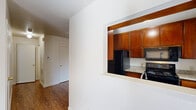 This efficient single-floor, one-bedroom, one-bathroom unit offers a thoughtfully organized layout across a compact but functional footprint. The open living area is a standout, featuring warm hardwood-style flooring that runs throughout the main living spaces, bright white walls, and a sliding glass door that floods the room with natural light while providing direct outdoor access. A ceiling fan in the living area adds to the overall comfort.

The kitchen is accessible via a distinctive pass-through window opening from the living area, creating a connected feel. Inside, the kitchen features rich warm-toned wood cabinetry, granite-style countertops, black appliances including a range and refrigerator, and a window overlooking the exterior — providing both natural light and ventilation.

The bedroom is a comfortable, carpeted retreat equipped with a ceiling fan, a window with blinds, and a generously sized closet, offering ample storage. The neutral tones throughout promote a calm and restful atmosphere.

The bathroom is clean and well-equipped, featuring a full tub/shower combination with grab bars, a granite-topped vanity with a wood cabinet base, and hardwood-style flooring that ties in with the rest of the unit. A hallway connects the main spaces, completing this practical and cohesive residential layout.
