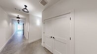 This well-appointed 2-bedroom, 2-bathroom residence in Warrenville, SC offers a contemporary design defined by polished concrete floors, crisp white walls, and matte black hardware and fixtures throughout. The open-concept living and kitchen area is anchored by a gray kitchen island with a granite countertop, complemented by white shaker cabinetry, a subway tile backsplash, stainless steel appliances, and a black matte faucet. Large windows flood the living area with natural light and offer views of the surrounding brick architecture and landscaping, while an oversized ceiling fan adds both function and style. A hallway with modern pendant and sconce lighting connects the living space to the private quarters. Both bedrooms are generously sized, each equipped with ceiling fans and ample closet space. The two bathrooms carry the same clean aesthetic, featuring granite vanities and dark cabinetry. The primary bath includes a glass-enclosed walk-in shower with white subway tile, while the secondary bath offers a full tub-shower combo. Matte black accents tie the design together cohesively throughout the entire residence, creating a modern industrial ambiance.