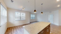 This single-floor residence showcases a thoughtfully designed open-concept layout that seamlessly connects the kitchen, dining, and living areas. The kitchen serves as a central focal point, featuring a large granite-topped island illuminated by two elegant pendant lights. Two-toned cabinetry — combining light wood upper cabinets with darker lower units — pairs with a full suite of stainless steel appliances, including a refrigerator, range, microwave, and dishwasher. Light wood-style flooring runs throughout the main living areas, contributing to a clean, contemporary aesthetic.

Multiple windows fitted with horizontal blinds flood the space with natural light, creating a bright and airy atmosphere throughout. A track lighting fixture in the living area provides additional illumination. The bedrooms feature plush carpeting and ceiling fans, with ample natural light from well-placed windows. One bedroom includes a closet and connects conveniently to the hallway.

The bathroom is finished with matching granite countertops, warm wood-tone cabinetry, a single vanity with a large mirror, and a full tub-shower combination, all set on neutral tile flooring. The overall design maintains a cohesive, modern palette of warm neutrals and contemporary finishes throughout.