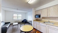 This 490 square foot apartment in Greenville, NC offers a practical living space on a single floor. The efficient layout maximizes the available area, featuring a kitchenette, bathroom, bedroom, and living area. The kitchenette is equipped with light-colored cabinetry, basic appliances, and a small dining area with a round table and chairs. The bathroom includes a standard tub-shower combination, toilet, and vanity. The bedroom accommodates a full-sized bed and basic furnishings, with carpeted flooring and a window providing natural light. The living area, also carpeted, offers space for seating and study. Throughout the apartment, white walls and ceiling contribute to a bright, open feel. Practical features include a water heater in a dedicated closet and built-in storage spaces. The hardwood flooring in the kitchen area adds a touch of warmth to the overall design. This compact apartment is well-suited for students or young professionals seeking affordable, no-frills city living in close proximity to local amenities.