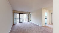 This single-floor residence is thoughtfully laid out to maximize both functionality and comfort. The living area serves as the heart of the home, featuring plush wall-to-wall carpeting, crown molding, and large sliding glass doors that open onto a balcony overlooking mature trees, allowing abundant natural light to fill the space. Sheer curtains frame the doors, adding a soft finishing touch. An adjacent window further enhances the bright, open feel of the room, while a nearby entry area connects seamlessly to the rest of the unit.

The galley-style kitchen is efficiently designed with ample white cabinetry extending to the ceiling, dark countertops, a single-basin sink, and white appliances including a gas range and refrigerator. Wood-look flooring runs throughout the kitchen, providing a clean contrast to the carpeted living spaces.

The bedrooms are generously proportioned, each featuring plush carpeting and windows with views of the surrounding greenery. The primary bedroom includes direct access to a walk-in closet and an en-suite bathroom. The bathroom is finished with wood-look flooring, a vanity with dark countertops, white cabinetry, and a tub-shower combination with tile surround.