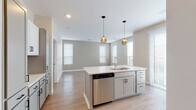 Located at 110 N Chestnut St in Olathe, Kansas, this single-story residence presents a clean, contemporary design characterized by neutral tones, light-toned luxury vinyl plank flooring, and plush carpeting in the bedrooms. The open-concept layout seamlessly connects the kitchen and living areas, creating a spacious and functional flow throughout the home.

The kitchen serves as a central hub, featuring a large center island with an undermount sink, crisp white quartz countertops, and gray shaker-style cabinetry with matte black hardware. Stainless steel appliances—including a range, microwave, and dishwasher—add a modern touch, while subway tile backsplash and two warm-toned pendant lights overhead contribute refined detail. Multiple windows allow natural light to fill the space generously.

The living area extends from the kitchen, offering an open and airy feel with wide windows fitted with blinds. Bedrooms are carpeted and well-proportioned, with at least one featuring a dedicated walk-in closet equipped with built-in shelving and hanging rods.

The bathrooms are finished with light wood-look flooring, gray vanity cabinetry, white quartz countertops, and tiled tub-shower combinations. The overall ambiance is bright, cohesive, and move-in ready.