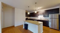 This Spring House apartment unit is a thoughtfully designed single-floor residence that combines modern finishes with comfortable, functional living spaces. The kitchen serves as a central highlight, showcasing rich dark cabinetry, granite countertops, and a full suite of stainless steel appliances including a refrigerator, microwave, range, and dishwasher. A central island with a granite surface provides additional prep space and adds to the open, airy feel of the area. Pendant lighting and a track light fixture illuminate the kitchen, which flows seamlessly into the living area. The living room features warm hardwood-style flooring, a ceiling fan, and French doors that invite natural light and outdoor views. The bedrooms are finished with plush carpeting, ceiling fans, and multiple windows fitted with blinds, allowing for ample natural light and ventilation. The bathroom is well-equipped with a soaking tub and tub surround finished in warm stone-toned tile, a dark vanity with granite countertops, and hardwood-style flooring. A spacious walk-in closet with built-in wire shelving provides generous storage. Throughout the unit, clean white walls and consistent finishes create a cohesive and inviting atmosphere.