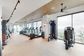 Located in the heart of Midtown Atlanta at 1081 Juniper St NE, this upscale fitness center offers a thoughtfully designed, single-floor layout that combines function with refined aesthetics. The entrance welcomes visitors with light hardwood flooring, vertical wood slat partitions, built-in shelving, and a clean, modern corridor that sets the tone for the space beyond.

The main workout floor is expansive and well-lit, featuring speckled tile flooring, a warm wood-paneled ceiling, and recessed lighting complemented by ceiling fans. Floor-to-ceiling windows line the perimeter, flooding the space with natural light and offering sweeping elevated views of the Atlanta skyline and surrounding cityscape. The gym is fully equipped with a comprehensive range of cardio machines — including treadmills, ellipticals, and stationary bikes — as well as strength training machines, cable systems, rowing machines, and free weights.

A dedicated studio area features spin bikes, a weight bench, and a vibrant art piece, creating an energetic yet refined workout environment. Large sliding glass doors connect to an outdoor area with a pool visible from within the gym. Mirrored walls and built-in storage further enhance the functionality of the space, while water fountains and clean sightlines throughout contribute to a polished, amenity-rich fitness experience.