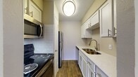 This one-floor apartment offers a blend of functionality and style. The galley kitchen boasts white cabinetry, stainless steel appliances, and a subway tile backsplash. The bathroom features a shower-tub combo and ample vanity space. The living area is carpeted and includes a ceiling fan, while large windows provide natural light. A unique vertical paneling accent wall adds character to one room. The overall design emphasizes clean lines and a neutral color palette, creating a modern and inviting living space.