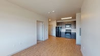 This single-floor unit offers a clean, modern layout that balances functionality with contemporary design. The open-concept living and kitchen area is anchored by light-toned hardwood-style flooring that runs throughout, creating a warm and cohesive aesthetic. The kitchen is well-equipped, featuring dark espresso-toned cabinetry with ample upper and lower storage, white countertops, a classic subway tile backsplash, and a full suite of black appliances including a refrigerator, electric range, microwave, and dishwasher. A stainless steel sink with a modern faucet completes the space. Overhead fluorescent lighting keeps the kitchen well-lit and practical.

The bedrooms are finished with neutral-toned carpet and include baseboard heating units for efficient climate control. A window in one bedroom allows natural light to filter in, offering views to the exterior. The rooms are generously proportioned with clean white walls and ceiling-mounted light fixtures.

The bathroom features a full-size tub and shower combination with a white surround unit equipped with built-in shelving, complemented by chrome fixtures and hardwood-style flooring. The overall unit maintains a neutral, move-in-ready aesthetic suited to a variety of living arrangements.