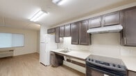 Located at 9050 Norfolk Blvd in Jacksonville, FL, this single-floor unit offers a thoughtfully designed, accessible living space with a clean, neutral aesthetic throughout. Light wood-style flooring runs through the main living areas, complementing the bright white walls and creating a warm, cohesive feel.

The open-concept layout connects the living area to the kitchen, which is well-appointed with rich dark espresso cabinetry, light countertops, a white refrigerator, a black electric range, and an under-cabinet range hood. The accessible counter design features open knee space beneath the sink, accommodating a variety of needs. Fluorescent lighting ensures the kitchen is bright and functional.

The spacious living room benefits from natural light through a large window with blinds and features a ceiling fan with integrated lighting. A textured ceiling adds character to the room.

Bedrooms include closets fitted with wire shelving systems for organized storage. One room features a bifold-door closet, while another offers a full-depth reach-in closet, both maximizing available storage.

The bathroom is designed with accessibility in mind, featuring stainless steel grab bars near the toilet, a wall-mounted vanity, light tile flooring, and a full shower area — all arranged for ease of use. A fire alarm system is also present throughout the unit, ensuring safety compliance.