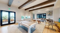 Located in Clermont, FL, this thoughtfully designed single-floor amenity space offers a generous footprint across two distinct living areas, blending modern aesthetics with comfortable, functional design.

The lounge area showcases soaring ceilings adorned with striking dark wood beam accents, light hardwood flooring, and a bright, neutral color palette. A built-in entertainment wall with open shelving, cabinetry, and a mounted flat-screen TV anchors the space, while plush seating arrangements — including oversized sofas and accent chairs — create inviting conversation areas. A wet bar with hexagonal tile backsplash, open shelving, and a dark wood counter adds a sophisticated touch, complemented by banquette seating with bold teal and yellow upholstery. Ample windows flood the space with natural light and offer views of the surrounding landscape.

The game room is equally well-appointed, featuring a sleek pool table, a foosball table, and a bar-height counter with seating. A vibrant living moss wall introduces a natural, artistic element, while large windows and glass double doors open to an outdoor terrace. Exposed wood beams continue throughout, maintaining a cohesive design language. Together, the two areas deliver a versatile, upscale environment ideal for both relaxation and recreation.
