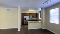 This multi-floor space is designed with functionality and style in mind. The kitchen serves as a central highlight, featuring rich dark wood cabinetry that extends to the ceiling, offering generous storage. Stainless steel appliances, including a French door refrigerator with an ice and water dispenser, a built-in microwave, and a gas range, provide a modern, cohesive look. The granite countertops add an elegant touch, extending to a peninsula that creates a natural boundary between the kitchen and the adjacent living area, while also offering additional prep and casual dining space. A built-in sink is positioned near a window, allowing natural light into the workspace. The flooring throughout is a dark hardwood-style material that grounds the space with warmth and visual continuity. Neutral, light-toned walls keep the space feeling open and bright. Track lighting in the adjoining area and overhead fluorescent lighting in the kitchen ensure the space is well-lit. The open layout between the kitchen and living areas promotes an easy flow, making the space well-suited for everyday living and entertaining across its three floors.