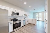 Located at 115 N 40th St in Omaha, Nebraska, this thoughtfully designed unit offers a bright and modern living experience within a compact, efficient floor plan. The open-concept kitchen and living area form the heart of the space, seamlessly connected to maximize functionality. The kitchen is outfitted with crisp white shaker-style cabinetry, matte black hardware, light quartz countertops, a classic subway tile backsplash, and a full suite of stainless steel appliances including a range, over-the-range microwave, dishwasher, and refrigerator. Pendant lighting and recessed fixtures illuminate the space, while an L-shaped counter layout provides ample prep and storage space. The living area extends naturally from the kitchen, bathed in natural light from large windows and French doors that open to an outdoor area, offering pleasant exterior views. A ceiling fan adds comfort to this airy zone. Light wood-tone luxury vinyl plank flooring runs consistently throughout, lending warmth and visual continuity. The bathroom features a white vanity with matte black hardware, a round mirror, a bathtub, and matching flooring for a clean, cohesive look. A dedicated closet provides practical storage. The overall aesthetic is clean, contemporary, and move-in ready.