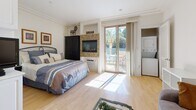 Located at 8020 W Manchester Ave in the desirable Playa del Rey neighborhood of Los Angeles, this thoughtfully designed single-level studio offers a seamless open-plan layout that maximizes every inch of its space. Light hardwood floors run throughout, lending warmth and continuity across all areas.

The main living area serves multiple functions with ease. A built-in granite-topped desk provides a dedicated workspace, while a cozy sitting area with a plush sofa offers a place to relax. A glass-top coffee table and wrought-iron dining set complete the central gathering space. A tiled fireplace serves as a stylish focal point, flanked by a built-in media niche. Floor-to-ceiling sliding glass doors flood the room with natural light and open directly onto a private outdoor patio, where views of mature palm trees add a quintessential Southern California ambiance.

The sleeping area is integrated into the open layout, with a dedicated wall-mounted TV niche and ample built-in cabinetry providing storage. In-unit stacked laundry is conveniently tucked nearby.

The kitchen features white shaker cabinetry, granite countertops with a stone tile backsplash, and a full suite of stainless steel appliances including a refrigerator, range, and microwave.

The bathroom is finished with large-format tile flooring and includes a shower-tub combination with a glass sliding enclosure. Track lighting throughout the space ensures bright, even illumination.