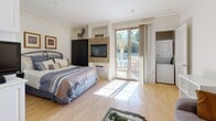 Located at 8020 W Manchester Ave in the desirable Playa del Rey neighborhood of Los Angeles, this thoughtfully designed single-level studio offers a seamless open-plan layout that maximizes every inch of its space. Light hardwood floors run throughout, lending warmth and continuity across all areas.

The main living area serves multiple functions with ease. A built-in granite-topped desk provides a dedicated workspace, while a cozy sitting area with a plush sofa offers a place to relax. A glass-top coffee table and wrought-iron dining set complete the central gathering space. A tiled fireplace serves as a stylish focal point, flanked by a built-in media niche. Floor-to-ceiling sliding glass doors flood the room with natural light and open directly onto a private outdoor patio, where views of mature palm trees add a quintessential Southern California ambiance.

The sleeping area is integrated into the open layout, with a dedicated wall-mounted TV niche and ample built-in cabinetry providing storage. In-unit stacked laundry is conveniently tucked nearby.

The kitchen features white shaker cabinetry, granite countertops with a stone tile backsplash, and a full suite of stainless steel appliances including a refrigerator, range, and microwave.

The bathroom is finished with large-format tile flooring and includes a shower-tub combination with a glass sliding enclosure. Track lighting throughout the space ensures bright, even illumination.