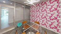 Located at 1270 Spring St NW in Atlanta's dynamic Midtown neighborhood, this single-floor commercial space makes a bold design statement from the moment you enter. The most striking feature is the vivid hot-pink wallpaper adorned with a repeating white animal motif, which covers multiple walls and instantly energizes the interior with a playful yet professional character.

The space is centered around a compact meeting area furnished with a round glass-top table and wood-and-metal chairs, creating an intimate setting ideal for small group collaboration or client meetings. A sculptural starburst chandelier with linear LED elements provides bright, focused overhead lighting that complements the modern aesthetic.

Floor-to-ceiling glass partitions and aluminum-framed glazed walls define the space while maintaining visual openness and transparency, allowing natural light to filter through from adjacent areas. The patterned carpet in muted grey tones grounds the space and balances the vibrancy of the wallpaper, while the neutral white ceiling and grey walls elsewhere provide a clean contrast.

The overall design is contemporary and intentional, blending bold artistic wallcoverings with sleek, minimalist furnishings. The combination of transparency through glass walls, vibrant accent décor, and functional meeting furniture makes this a distinctive and memorable workspace in the heart of Atlanta.