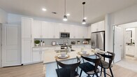 This single-floor, 2-bedroom, 2-bathroom residence offers a well-organized layout with modern finishes and a bright, cohesive aesthetic throughout. The open-concept kitchen and living area serves as the heart of the home, featuring crisp white shaker cabinetry extending to the ceiling, a geometric tile backsplash, light quartz countertops, and stainless steel appliances including a refrigerator, range, and over-the-range microwave. A central island with seating provides both prep space and casual dining. Light wood-tone flooring runs through the main living areas, and in-unit laundry is conveniently tucked nearby. The living room is bright and welcoming, with large windows that invite natural light and a ceiling fan overhead. Both bedrooms feature plush carpet, soft sage green accent walls, and windows with outdoor views of lush greenery, creating a calm and restful atmosphere. The generously sized primary bedroom includes a dedicated closet. The primary bathroom offers a long vanity with white cabinetry, a glass-enclosed shower with marble-style tile, and a separate water closet. The second bathroom features a tub-shower combination with elegant stone-patterned tile surround and a matching white vanity. Two closets provide ample storage throughout this well-designed residence.