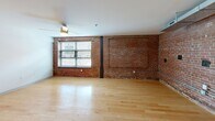 Located at 1700 Fairview St in Greensboro, NC, this 2-bedroom, 1-bathroom loft-style residence showcases a compelling blend of industrial character and modern finishes across a single floor. The open living room is anchored by striking exposed brick walls, light hardwood flooring, and a ceiling fan, with windows allowing natural light to brighten the space. The kitchen is well-equipped, featuring rich dark-espresso cabinetry, granite-look countertops, a double stainless steel sink, and a full suite of black appliances including a refrigerator, range, microwave, and dishwasher. Exposed ductwork overhead adds to the loft's industrial aesthetic. The primary bedroom continues the exposed brick motif, complemented by plush carpeting, a ceiling fan, and ample room to accommodate furnishings. The second bedroom also features carpet flooring and a ceiling fan, offering a comfortable and versatile space. Three hallways connect the layout efficiently, while two closets provide dedicated storage. The bathroom is clean and functional, finished with marble-look tile flooring, a soaking tub with shower, and chrome fixtures. The overall ambiance is distinctly urban, combining raw architectural elements with thoughtful modern updates throughout.