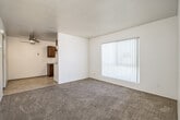 Located at 1917 F Ave in National City, CA, this one-bedroom, one-bathroom unit offers a practical and efficient single-floor layout. The living area is finished with plush carpeting and features a large window dressed with vertical blinds, allowing natural light to fill the space. It connects openly to the kitchen, which is finished with light wood-look flooring, rich dark-wood cabinetry, a stainless sink, and white appliances including an electric range and refrigerator, complemented by an overhead range hood. A ceiling fan provides additional comfort in the kitchen area. The bedroom is a comfortable size, carpeted, and includes a sliding-door closet with built-in shelving for organized storage. A window with vertical blinds brings in natural light, keeping the room bright and airy. The bathroom is clean and simply appointed, featuring a full tub-shower combination with white surround and built-in shelving, light wood-look flooring, a white vanity, and chrome fixtures. A hallway connects the main areas, contributing to the unit's straightforward and functional flow. The overall aesthetic is neutral and move-in ready, with white walls and light finishes throughout.