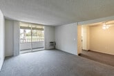 Located at 10320 Warner Ave in Fountain Valley, California, this two-bedroom, two-bathroom residence offers a functional and well-organized single-floor layout. The living room features neutral carpet, a textured ceiling, and a wall-mounted HVAC unit, opening directly onto a private balcony through sliding glass doors that let in natural light and provide pleasant outdoor views of the surrounding greenery. The living area flows into the dining space, which connects to a galley-style kitchen equipped with white cabinetry, dark countertops, a stainless steel sink, an electric range, and wood-look flooring beneath a skylight that brightens the room. Both bedrooms are carpeted and feature closets — one with sliding doors and a window fitted with vertical blinds allowing natural light. The primary bedroom is generously sized with its own access to a bathroom that includes a vanity with storage cabinetry and a mirror. The second bathroom offers a full tub-shower combination with wood-look flooring. A dedicated entrance and two closets throughout the unit provide practical storage solutions. The overall ambiance is clean, bright, and neutral, making it a versatile and move-in ready space.