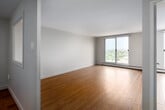 Located on an upper floor at 10 Overlea Dr in Kitchener, Ontario, this one-bedroom, one-bathroom unit offers a practical and well-organized layout with consistent hardwood flooring throughout. The open living area is bright and airy, anchored by a large sliding glass door that frames sweeping elevated views of the Kitchener cityscape and surrounding greenery, allowing natural light to fill the space generously.

The galley-style kitchen is efficiently designed, featuring white cabinetry both above and below the counter, a neutral countertop with an integrated sink, a tile backsplash, and full-size appliances including a refrigerator and dishwasher. A dedicated door within the kitchen provides additional access or storage utility.

The bedroom is a comfortable size, offering a closet with a full-width hanging rod for organized storage, and is finished with the same warm hardwood flooring found throughout the unit. Neutral light-toned walls in every room contribute to a clean, understated aesthetic.

The bathroom includes a full-size soaking tub with an overhead shower, tiled surround walls, and chrome fixtures. Baseboard heating is present throughout the unit. Overall, the space presents a functional and straightforward layout suited for comfortable everyday living.