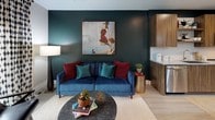 This thoughtfully designed 1-bedroom, 1-bathroom residence offers a seamless open-concept layout finished with light hardwood-style flooring throughout. The kitchen is a standout feature, boasting rich walnut-toned cabinetry, granite countertops, a white subway tile backsplash, and a full suite of stainless steel appliances including a refrigerator, range, microwave, and dishwasher. A large kitchen island with pendant lighting provides additional prep space and casual seating, making it ideal for both cooking and entertaining. The living area is anchored by a bold teal accent wall, large sliding glass doors that invite abundant natural light and outdoor views, and ample room for comfortable seating arrangements. The bedroom is a calm retreat, featuring a dramatic dark accent wall, large windows with outdoor views, and generous natural light. The full bathroom connects conveniently to the bedroom corridor and includes a granite-topped vanity with warm wood cabinetry, a soaking tub with tiled surround, and a separate shower. Recessed lighting, clean white trim, and a neutral color palette tie the entire residence together into a cohesive, modern aesthetic.