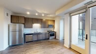 This thoughtfully laid-out 1-bedroom, 1-bathroom unit offers an efficient and modern living experience across a single floor. The open-concept kitchen is a standout feature, equipped with a full suite of stainless steel appliances including a refrigerator, electric range, built-in microwave, and dishwasher. Dark-toned cabinetry contrasts cleanly against a classic white subway tile backsplash, while track lighting overhead ensures the space is well-lit. Hardwood-style flooring flows throughout the main living and kitchen areas, adding warmth and continuity.

A hallway connects the main living space to the bedroom, bathroom, and closet, with clean white walls and recessed lighting maintaining a bright, airy feel throughout. The bedroom features neutral-toned carpet and is painted in soft, calming hues, providing a comfortable retreat. The bathroom is finished with wood-look tile flooring and includes a combined tub and shower, toilet, and a chrome towel bar.

A dedicated closet provides practical storage, while a glass sliding door off the kitchen opens to a private outdoor balcony, allowing for natural light and outdoor views. The overall aesthetic is clean, contemporary, and functional, making efficient use of the available space.