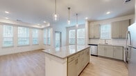 This thoughtfully designed single-floor residence offers a seamless blend of modern aesthetics and functional living. Light wood-tone flooring flows consistently throughout the space, complemented by crisp white walls and recessed lighting that create a clean, airy ambiance.

At the heart of the home, the kitchen is a standout feature with sage-toned shaker-style cabinetry, granite countertops, a white subway tile backsplash, and a full suite of stainless steel appliances including a range, microwave, dishwasher, and refrigerator. A central island with a granite top and pendant lighting above serves as both a prep space and a natural gathering point, opening directly to the living area.

The living room is bathed in natural light, courtesy of multiple windows fitted with blinds that frame views of the surrounding greenery. A tray ceiling adds architectural interest and depth to the space.

The bedroom is a comfortable, well-lit retreat with windows overlooking the exterior, providing ample natural light. It connects directly to the full bathroom, which features a granite-topped double vanity with sage cabinetry, a glass-enclosed shower, and direct access to a walk-in closet outfitted with built-in shelving. A utility room and hallway complete the layout, ensuring practical storage and circulation throughout.