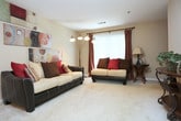 This single-story home in Lithonia, Georgia offers a thoughtfully arranged floor plan with multiple living spaces finished in warm, neutral tones. The living room serves as the central gathering area, featuring plush carpeting, a textured ceiling, and a large window dressed with draping curtains that invite natural light and views of the surrounding greenery.

The galley-style kitchen is efficiently designed with white countertops, wood-trimmed cabinetry, and hard-surface flooring. It opens directly into a dedicated dining area illuminated by a chandelier, creating a natural flow between cooking and dining spaces.

The primary bedroom includes carpet flooring, a ceiling fan, and direct access to an en-suite bathroom featuring a wide vanity with an extended countertop and a large wall mirror. Additional bedrooms are carpeted, well-lit by windows, and provide comfortable proportions for various uses.

The bathrooms throughout the home maintain a consistent, clean aesthetic, each equipped with a tub-shower combination, hard-surface flooring, and vanity storage. The overall design emphasizes functional living with consistent finishes, making this a practical and comfortable single-floor residence.