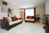 This single-story home in Lithonia, Georgia offers a thoughtfully arranged floor plan with multiple living spaces finished in warm, neutral tones. The living room serves as the central gathering area, featuring plush carpeting, a textured ceiling, and a large window dressed with draping curtains that invite natural light and views of the surrounding greenery.

The galley-style kitchen is efficiently designed with white countertops, wood-trimmed cabinetry, and hard-surface flooring. It opens directly into a dedicated dining area illuminated by a chandelier, creating a natural flow between cooking and dining spaces.

The primary bedroom includes carpet flooring, a ceiling fan, and direct access to an en-suite bathroom featuring a wide vanity with an extended countertop and a large wall mirror. Additional bedrooms are carpeted, well-lit by windows, and provide comfortable proportions for various uses.

The bathrooms throughout the home maintain a consistent, clean aesthetic, each equipped with a tub-shower combination, hard-surface flooring, and vanity storage. The overall design emphasizes functional living with consistent finishes, making this a practical and comfortable single-floor residence.