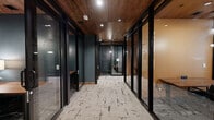 Located at 2121 S Broadway in Denver, Colorado, this thoughtfully designed commercial space offers a refined blend of modern aesthetics and functional workspaces across a single floor. The layout balances private and collaborative environments seamlessly, catering to a variety of professional needs.

A welcoming reception area greets visitors with plush seating, a rich wood-paneled ceiling, and a wall-mounted display screen — setting an immediate tone of sophistication. Glass-partitioned private offices line a corridor finished with the same warm wood ceiling and patterned carpeting, offering both transparency and privacy.

A formal conference room features a substantial wood table surrounded by upholstered chairs, with floor-to-ceiling windows that invite abundant natural light and views of the surrounding neighborhood. Equally distinctive are the architecturally designed booth-style collaboration nooks, framed by custom wood house-shaped structures with slatted detailing and pendant lighting — providing intimate settings for informal meetings or focused work.

A well-appointed kitchenette serves the space with a sleek countertop, integrated sink, stainless steel appliances, a smart beverage station, and elegant wall sconces against a tiled backsplash. Throughout the space, curated art pieces, including geometric wood panel triptychs, and lush greenery contribute to a warm, creative atmosphere that is both professional and inviting.