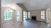 This single-story residence showcases a thoughtfully designed open layout with a neutral color palette and a variety of finishes that complement each room. The living area is a standout feature, boasting dramatic vaulted ceilings with a textured finish, dark wood-style plank flooring, and a tiled fireplace that serves as a focal point. Multiple windows and a glass-paned door allow abundant natural light to fill the space while providing direct access to an outdoor balcony, offering views of surrounding greenery.

The open-concept design connects the living area seamlessly to the kitchen and dining space. The kitchen is well-appointed with white cabinetry, light countertops, a grey subway tile backsplash, stainless steel appliances including a built-in microwave and electric range, and wood-style flooring. A window above the counter brings in additional natural light.

The bedrooms feature plush carpeting, ceiling fans, and windows with blinds. One bedroom includes built-in wall shelving, adding functional storage. The bathroom is clean and functional, offering a white vanity with an undermount sink, a combined tub and shower with white tile surround, and wood-style flooring that ties the space together cohesively.