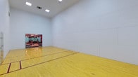 Located in Addison, this dedicated racquetball court offers a well-appointed space designed for both competitive and recreational athletic use. The court features a gleaming, polished hardwood floor with clearly marked court lines, providing excellent traction and visibility during play. The walls are finished with smooth, seamless white paneling that spans floor to ceiling, meeting official standards for consistent ball rebound and play. Soaring ceilings contribute to a spacious, open feel, allowing full range of movement without restriction. Recessed overhead lighting illuminates the entire court evenly, minimizing shadows and ensuring optimal visibility. A mirrored wall section near the entry connects the court visually to an adjacent fitness area, offering a glimpse of additional workout equipment. The clean, minimalist design keeps the focus squarely on athletic performance. The single-floor layout ensures straightforward accessibility, making this court a convenient and functional facility for players of all skill levels.