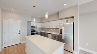 Located at 20350 North 7th Avenue in Phoenix, Arizona, this efficiently designed single-floor unit offers a thoughtfully organized open-concept layout that seamlessly combines the kitchen and living area into one cohesive space. Light wood-look flooring runs throughout, lending warmth and visual continuity across the entire floor plan.

The kitchen is a standout feature, showcasing a two-tone cabinetry design with crisp white upper cabinets and charcoal gray lower cabinets, complemented by a neutral tile backsplash. A large quartz-topped island provides additional prep and gathering space, while stainless steel appliances — including a French door refrigerator, dishwasher, microwave, and range — add a polished, modern finish. Stylish pendant lights hang above the island, enhancing the contemporary aesthetic.

The living area is bright and airy, benefiting from large sliding glass doors and oversized windows that flood the space with natural sunlight and offer outdoor views. A ceiling fan ensures year-round comfort.

The bathroom is clean and modern, featuring a full glass-enclosed walk-in shower with large-format tile surround, a wall-mounted vanity with a white countertop, and light wood flooring that echoes the rest of the unit. The overall design palette of soft neutrals and modern finishes creates a cohesive, move-in-ready environment.