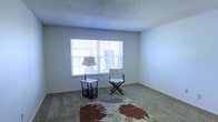 This single-floor space presents a straightforward and practical layout designed for comfortable everyday living. The interior is finished with wall-to-wall carpeting that adds warmth underfoot, complemented by neutral-toned walls that create a calm and versatile backdrop throughout. The textured ceiling adds a subtle architectural detail consistent across the space. A notable feature is the large window that allows ample natural light to filter into the main living area, brightening the room and creating an open, airy feel. The window is fitted with horizontal blinds, offering adjustable light control and privacy. The living area is modestly proportioned yet functional, with enough space to accommodate seating and accent furnishings comfortably. The clean lines of the baseboards and the simplicity of the overall design give the space a tidy, well-maintained appearance. The neutral palette throughout makes the space highly adaptable to a variety of interior styles and furnishing choices. Overall, this single-story space offers a welcoming and low-maintenance environment with key features that support comfortable, day-to-day living.
