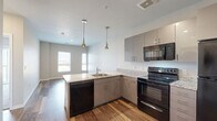 Located at 5730 W 89th Ave in Westminster, CO, this efficiently designed one-bedroom, one-bathroom unit offers a well-appointed single-floor layout. The open-concept kitchen and living area serves as the heart of the space, featuring wood-look flooring, gray flat-front cabinetry with brushed nickel hardware, granite-style countertops, and a full suite of black appliances including an electric range, over-the-range microwave, dishwasher, and refrigerator. Elegant pendant lighting hangs above the kitchen peninsula, which also houses a stainless steel sink. The living area benefits from natural light through large windows, creating a bright and welcoming atmosphere. The bedroom is carpeted for comfort, with a large sliding glass door that invites additional natural light and outdoor views, complemented by a dedicated closet with built-in rod storage. The full bathroom is finished with the same granite-style countertop, dark cabinetry, wood-look flooring, and a tub/shower combination. A stacked in-unit washer and dryer is also included, adding everyday convenience. Neutral wall tones throughout lend a clean, modern aesthetic to the entire space.