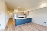 Located at 5127 Labounty Rd in Ferndale, WA, this thoughtfully designed 2-bedroom, 2-bathroom residence offers a clean, modern aesthetic across a single floor. The open-concept living and kitchen area serves as the heart of the home, featuring light wood-look flooring, recessed lighting, and a striking peninsula with a bold navy base and white countertop — ideal for casual dining or entertaining. The kitchen is well-appointed with two-tone cabinetry in gray tones, stainless steel appliances including a refrigerator, range, and microwave, and ample upper and lower cabinet storage. A bank of triple windows in the living area floods the space with natural light and provides views of the surrounding landscape. A central hallway connects the bedrooms and bathrooms, maintaining a clear and functional layout. Both bedrooms feature plush carpet flooring and sliding closet doors, offering comfortable, private retreats. The bathrooms are finished in a clean, minimal style with light flooring and dark cabinetry. A dedicated laundry room houses a full-size Whirlpool washer and dryer with overhead shelving, adding everyday convenience. The overall design is bright, neutral, and move-in ready.