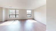 Located at 1 Uptown Cir in Normal, IL, this well-appointed 2-bedroom, 2-bathroom residence offers a thoughtfully designed single-level floor plan with a clean, contemporary aesthetic. The open-concept kitchen and living area serves as the heart of the home, featuring rich dark wood cabinetry, light stone countertops, stainless steel appliances including a gas range and French door refrigerator, and elegant pendant lighting over the kitchen island. Warm hardwood flooring flows throughout the main living areas, complementing the bright, neutral color palette. The spacious living room is bathed in natural light through large floor-to-ceiling windows that frame views of the surrounding Uptown neighborhood. Both bedrooms are generously sized, with soft carpet flooring, built-in closet storage, and large windows that continue the home's emphasis on natural light. The primary bathroom features a floating double vanity with stone countertops, a large mirror, and a walk-in glass shower, while the secondary bathroom includes a full soaking tub with tile surround. A hallway connects all rooms efficiently, and dedicated closet space adds practical storage. The overall ambiance is modern, clean, and inviting.