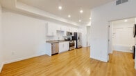 This well-designed single-floor unit offers a clean, modern aesthetic throughout, characterized by crisp white walls, light hardwood flooring, and recessed lighting that create a bright and inviting atmosphere. The kitchen is a standout feature, boasting sleek white cabinetry extending to the ceiling, granite countertops, a double-basin sink, and a full suite of stainless steel appliances including a gas range, over-the-range microwave, dishwasher, and a French door refrigerator with an ice maker. A hallway from the kitchen leads to the main entrance, keeping the layout efficient and well-organized. The open living area is generously proportioned, filled with natural light, and anchored by a ceiling fan. A sliding glass door opens onto a private balcony with views of the surrounding neighborhood, seamlessly blending indoor and outdoor living. A dedicated in-unit laundry area accommodates a stacked washer and dryer, adding everyday convenience. The bathroom is finished in a clean, minimalist style with a soaking tub, shower combination, built-in shelving, and matching light hardwood flooring. Throughout the unit, the consistent use of neutral tones and modern finishes contributes to a cohesive and polished living environment.