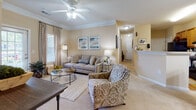 This single-floor, 2-bedroom, 2-bathroom residence offers a thoughtfully designed layout with warm neutral tones and classic finishes throughout. The living room serves as the heart of the home, featuring crown molding, a ceiling fan with light kit, plush carpeting, and a window that invites natural light. It connects seamlessly to both the dining area and the entry hallway, creating an open and accessible flow.

The dining area is a defined space accented by a chandelier, chair-rail molding, and decorative mirrors, lending it an elegant yet approachable character. Adjacent to it, the kitchen is equipped with warm wood cabinetry, light countertops, and black appliances including a range and refrigerator, complemented by hardwood flooring.

A central hallway with textured ceilings and flush-mount lighting connects the main living spaces to both bedrooms. The primary bedroom is generously proportioned with plush carpet, a ceiling fan, multiple windows, and direct access to an en-suite bathroom featuring a extended vanity with wood cabinetry and a shower-tub combination. The second bedroom is equally comfortable, with natural light and soft carpet. The second full bathroom mirrors the same classic design with hardwood flooring and a tub-shower combo.