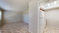 This single-floor space offers a practical and comfortable layout with tile flooring carried consistently throughout. The living area greets you with a large front-facing window that invites natural light, creating a bright and open atmosphere. A ceiling fan in the adjacent room adds comfort and airflow, complementing the window with blinds in that space as well.

The galley-style kitchen is a standout feature, finished with warm wood cabinetry, granite countertops, and a tile backsplash that combines classic marble-look tiles with a decorative mosaic accent. White appliances, including a refrigerator and a range with overhead ventilation, are neatly integrated into the layout. A skylight above the kitchen further enhances the natural brightness of the space.

A hallway connects the main living areas to the private rooms. The bedroom is a comfortable, well-sized room featuring light-toned tile flooring, a ceiling fan with integrated lighting, a window for natural light, and access to a spacious walk-in closet fitted with built-in shelving and hanging rods.

The bathroom is cleanly designed with tile flooring, a vanity with a light countertop, warm-toned wall tiles in the shower area, and brushed nickel fixtures throughout. The overall layout is efficient and functional, making good use of the available space across all rooms.