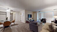 Located at 38360 Tamarac Blvd in Willoughby, Ohio, this single-floor residence offers a thoughtfully designed layout with comfortable living spaces throughout. The generously sized living room is a central highlight, featuring plush wall-to-wall carpeting, a wall-mounted television, and a large sliding glass door dressed with vertical blinds that floods the room with natural light. The open layout accommodates multiple seating arrangements, creating a versatile and welcoming atmosphere. The kitchen is equipped with light wood cabinetry, ample counter space, an electric range, and an over-the-range microwave, providing a practical and functional cooking environment. The residence includes multiple bedrooms, each carpeted and designed for comfort. The primary bedroom features a closet with bifold doors and is complemented by warm, neutral tones. A second bedroom offers a window with blinds, allowing for natural light and ventilation. The bathrooms include a vanity with light wood cabinetry, a large mirror, tile flooring, and a separate enclosed shower with textured glass doors. A hallway connects the private areas of the residence, offering convenient access to all rooms. Overall, the space presents a clean, neutral palette with a calm and livable ambiance throughout.