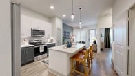 Located at 7200 N State Highway 360 in Grand Prairie, TX, this 1-bedroom, 1-bathroom residence offers a thoughtfully designed open-concept layout with modern finishes throughout. Light wood-style flooring flows seamlessly across the entire space, creating a cohesive and inviting atmosphere.

The kitchen is a standout feature, showcasing two-tone cabinetry with crisp white upper cabinets and deep navy-blue lower cabinets, complemented by white quartz countertops and a textured tile backsplash. A central island with bar seating and pendant lighting serves as both a functional workspace and a casual dining area. Stainless steel appliances, including a French door refrigerator, range, and over-the-range microwave, complete the well-equipped kitchen. An adjacent pantry provides additional storage.

The open living room benefits from large windows that fill the space with natural light and features a ceiling fan for added comfort. A soft blue-green accent wall adds a calming, contemporary touch to the living area.

The bedroom is a serene retreat with large windows, a ceiling fan, and direct access to a well-organized walk-in closet. The bathroom features a wide navy-blue vanity, white quartz countertop, a large mirror, and a shower-tub combination. Three closets throughout the unit offer generous storage solutions for everyday living.