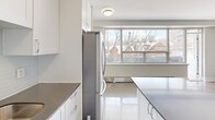Located at 66 Spadina Rd in Toronto's sought-after Annex neighbourhood, this one-bedroom, one-bathroom unit offers a well-considered layout across a single floor. The modern kitchen is equipped with stainless steel appliances — including a large French-door refrigerator, electric range with built-in microwave, and dishwasher — complemented by white cabinetry, dark countertops, and a subtle tile backsplash. Light-coloured porcelain tile flooring runs throughout the kitchen, which benefits from a large window that frames views of the surrounding rooftops and skyline. The living area flows naturally from the kitchen and features warm parquet flooring that adds character to the space. The bedroom is a comfortable size, with its own large window offering bright, open views over the neighbourhood's historic rooftops and the Toronto skyline beyond, along with a baseboard heating unit beneath. The bathroom is finished with classic white subway tile surrounding a full soaker tub with overhead shower. A private balcony extends the living space outdoors, while a hallway connects the unit's rooms with practical flow. Natural light is a consistent feature throughout the unit.