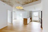 Located at 2600 Cavendish Boulevard in Montréal, this well-appointed 3-bedroom, 2-bathroom unit blends industrial character with contemporary finishes throughout its thoughtfully designed single floor. The open-concept kitchen and living area serves as the heart of the home, featuring a striking central island with a wood-panelled base and clean countertop, white upper cabinetry, stainless steel appliances, and track lighting overhead. A distinctive exposed concrete column anchors the kitchen space, complemented by a raw concrete ceiling detail that adds an urban, loft-inspired aesthetic. Light hardwood flooring flows seamlessly throughout the entire unit, enhancing the bright and airy atmosphere created by multiple windows that frame views of the surrounding neighbourhood. The three bedrooms are well-proportioned and filled with natural light, each featuring crisp white walls and the same warm hardwood floors. The primary bedroom offers a sliding glass door with an exterior view. The two bathrooms are finished in a clean, modern style, with one featuring a floating vanity, mirrored medicine cabinet, and a full tub-shower enclosure with tile surround. A clean hallway with ceiling access panels connects the private areas of the unit, completing this functional and stylish Montréal residence.