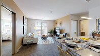 This single-floor residence offers a thoughtfully designed open-concept layout that seamlessly connects the living, dining, and kitchen areas. The living room is a welcoming space finished with plush carpet flooring, warm neutral-toned accent walls, and a sliding glass door that opens to a private balcony overlooking urban surroundings, filling the room with natural light.

The galley-style kitchen is outfitted with stainless steel appliances, including a refrigerator, range, and microwave, complemented by dark wood cabinetry, light countertops, and light wood-tone flooring that adds warmth to the space.

Two well-proportioned bedrooms each feature large windows that draw in abundant natural light and offer views of the surrounding cityscape. Both rooms are finished with soft carpet flooring and neutral walls that create a calm, restful atmosphere.

The unit includes two bathrooms. The primary bathroom features a sliding glass-door walk-in shower with built-in shelving, light wood-tone flooring, and a dark vanity with a clean white countertop. The second bathroom mirrors the modern aesthetic with a tub-shower combination, matching vanity finishes, and light flooring throughout.