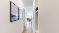 Located at 10410 Sam Furr Road in Huntersville, NC, this well-appointed 2-bedroom, 4-bathroom single-floor residence offers a thoughtfully designed layout with contemporary finishes throughout. Light wood-tone flooring flows seamlessly across the entire space, complemented by crisp white walls and black hardware accents that lend a modern, cohesive aesthetic.

The entrance leads down a bright hallway into an open-concept living, dining, and kitchen area filled with natural light from large windows dressed in sheer curtains and wood blinds. The kitchen features two-tone gray and white cabinetry, quartz countertops, stainless steel appliances, and a central island with seating — ideal for both cooking and casual dining. The dining area accommodates a full table beside generous windows, while the living room offers a comfortable, airy atmosphere.

Both bedrooms are accented by striking teal feature walls, with the primary bedroom showcasing elegant panel molding detail and ample natural light. Each bedroom is served by its own well-finished bathroom; the bathrooms include a dual-vanity option with gray cabinetry and a soaking tub with shower combination. Additional amenities include a dedicated laundry room, utility room, and two closets. A private balcony overlooks manicured landscaping and mature trees, offering a peaceful outdoor retreat.