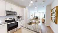 This single-floor residence showcases a thoughtfully designed open-concept layout that seamlessly connects the kitchen, dining, and living areas. The kitchen is a standout feature, outfitted with crisp white shaker cabinetry, granite countertops with subtle grey and white veining, a subway tile backsplash, and a full suite of stainless steel appliances including a French door refrigerator, electric range, and built-in microwave. A kitchen island with an undermount sink and brushed gold faucet serves as both a functional workspace and a natural gathering point, illuminated by pendant lighting overhead.

The living area extends naturally from the kitchen, bathed in natural light from large windows dressed with neutral drapes. A distinctive arched doorway adds architectural character, providing a graceful transition into the dining space. Warm hardwood-style flooring flows throughout the main living areas, complementing the light, neutral color palette.

The bedrooms offer a calm, restful atmosphere, with plush carpeting, ceiling fans, and windows that invite natural light. The primary suite includes access to a bathroom and a dedicated walk-in closet with built-in shelving, providing generous storage. Throughout, the space maintains a cohesive, modern aesthetic with warm gold accents and clean finishes.