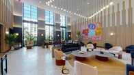 Located along Biscayne Boulevard in Miami, FL, this stunning lobby space makes an immediate impression with its soaring double-height ceilings and expansive floor-to-ceiling windows that flood the interior with natural light and offer views of lush tropical surroundings. The patterned mosaic tile flooring extends throughout, unifying the space with a refined, textural elegance.

At the heart of the lobby, a grand reception desk crafted from rich warm wood is framed by a series of distinctive rounded arches with mahogany-toned trim — a signature architectural detail repeated throughout the corridors and passageways, lending the space a bold, sculpted character. The coffered ceiling above the reception area features layered lighting that adds depth and warmth.

The main lounge area is thoughtfully curated with a mix of plush seating, including deep navy sofas, curved cream armchairs, and sculptural side tables with marble and glass surfaces. Suspended globe pendant lights cascade dramatically from the ceiling, creating an ambient glow. Large-scale contemporary paintings in vivid pinks, reds, and yellows animate the wood-paneled accent walls, providing striking focal points throughout.

Secondary seating nooks offer quieter, intimate settings with custom banquette seating and individual accent chairs. Tropical foliage punctuates the space, enhancing the Miami ambiance. The overall design balances bold artistic expression with refined, modern sophistication.